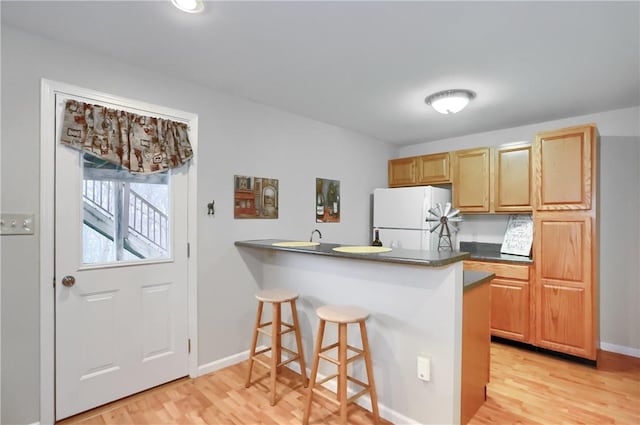 kitchen featuring kitchen peninsula, light wood-type flooring, and white fridge