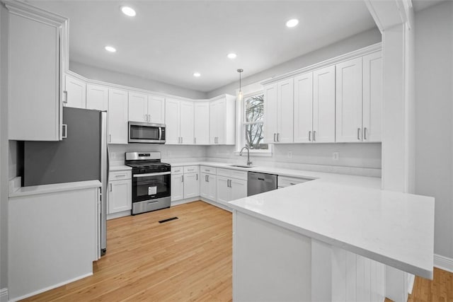 kitchen featuring sink, light hardwood / wood-style flooring, kitchen peninsula, white cabinets, and appliances with stainless steel finishes