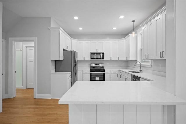 kitchen featuring kitchen peninsula, stainless steel appliances, sink, pendant lighting, and white cabinetry