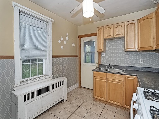 kitchen with ceiling fan, radiator heating unit, sink, light tile patterned flooring, and white gas range oven