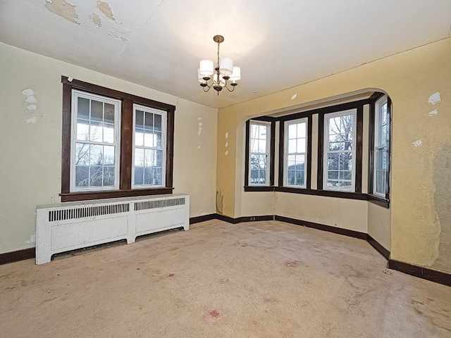 carpeted empty room featuring radiator and a notable chandelier