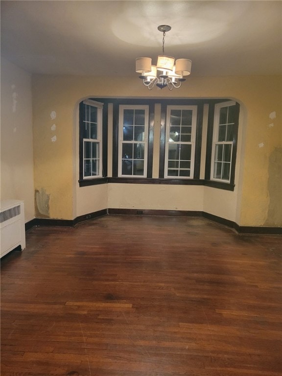 unfurnished dining area featuring a notable chandelier, dark wood-type flooring, and radiator