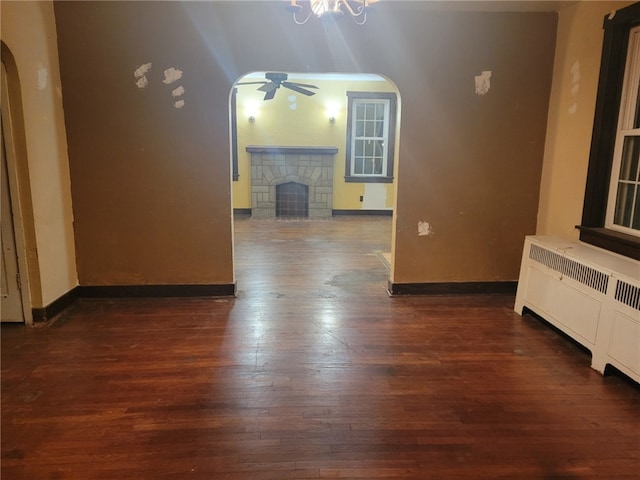 unfurnished living room with ceiling fan, dark hardwood / wood-style flooring, a fireplace, and radiator