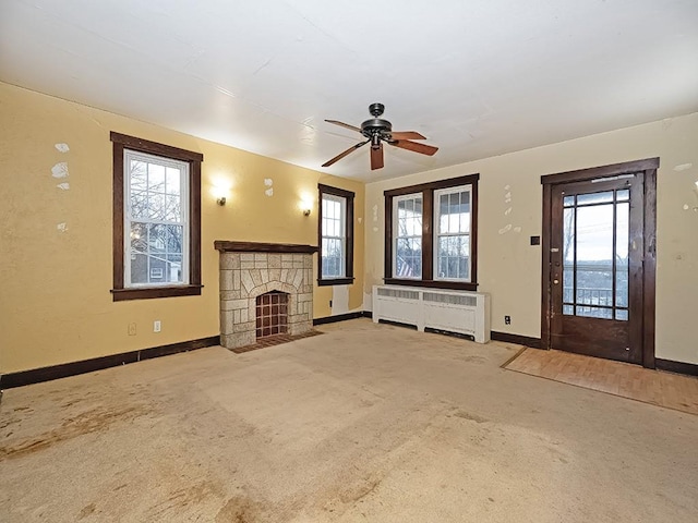 unfurnished living room featuring light colored carpet, a stone fireplace, radiator, and ceiling fan