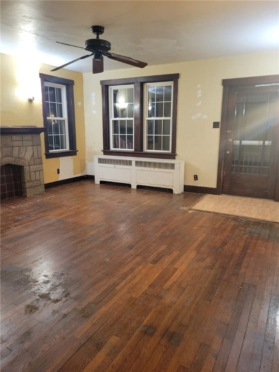 unfurnished living room with dark hardwood / wood-style floors, a stone fireplace, radiator, and ceiling fan