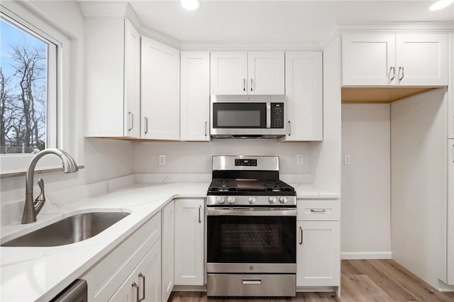 kitchen featuring white cabinets, stainless steel appliances, light stone counters, and sink