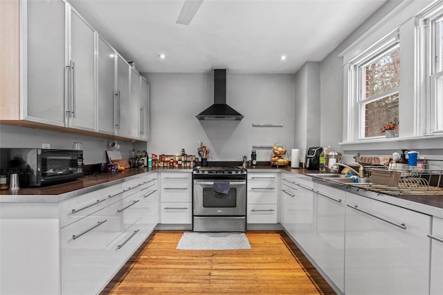 kitchen with light wood-type flooring, white cabinetry, wall chimney exhaust hood, and stainless steel range with gas stovetop