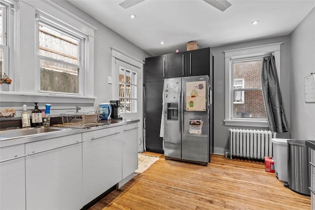 kitchen featuring radiator, white cabinetry, sink, stainless steel fridge with ice dispenser, and light hardwood / wood-style floors