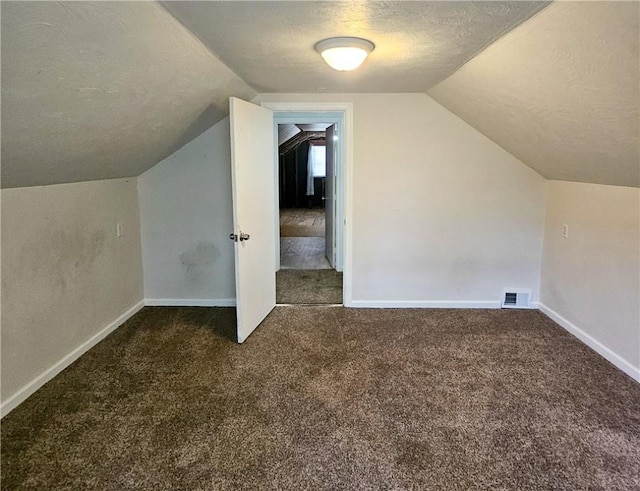 additional living space with dark colored carpet, a textured ceiling, and vaulted ceiling