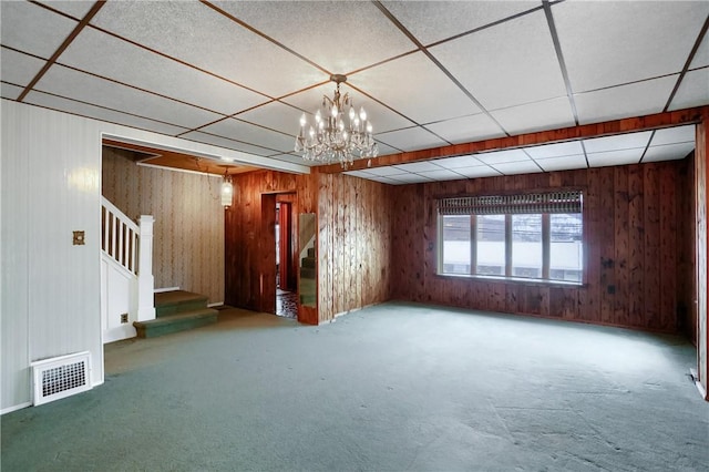 carpeted empty room featuring a drop ceiling and wooden walls