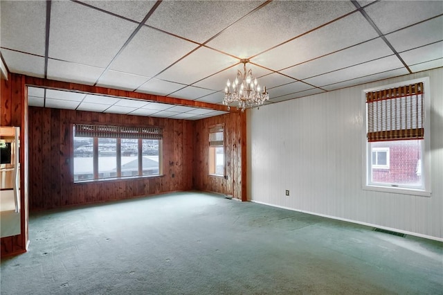 carpeted spare room with an inviting chandelier, a paneled ceiling, and wooden walls