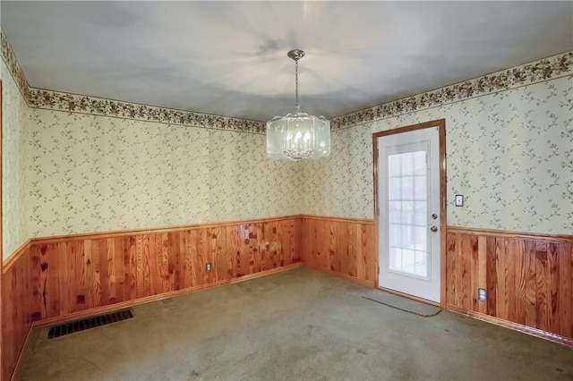 unfurnished dining area with wooden walls, a chandelier, and carpet floors