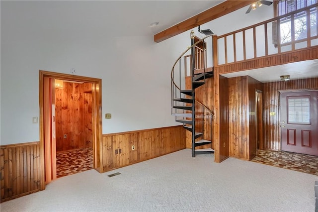 carpeted living room featuring beam ceiling, wooden walls, ceiling fan, and a towering ceiling