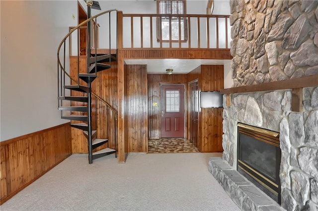 foyer with a stone fireplace, carpet, and wood walls