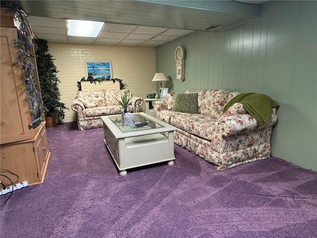 living room featuring dark colored carpet, a drop ceiling, and brick wall