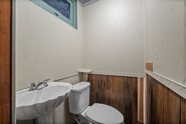 bathroom featuring wooden walls, sink, and toilet