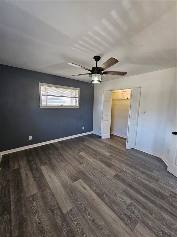 unfurnished bedroom featuring ceiling fan, a spacious closet, dark wood-type flooring, and a closet