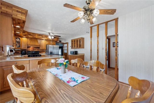 dining area featuring light wood-type flooring, a textured ceiling, ceiling fan, and sink