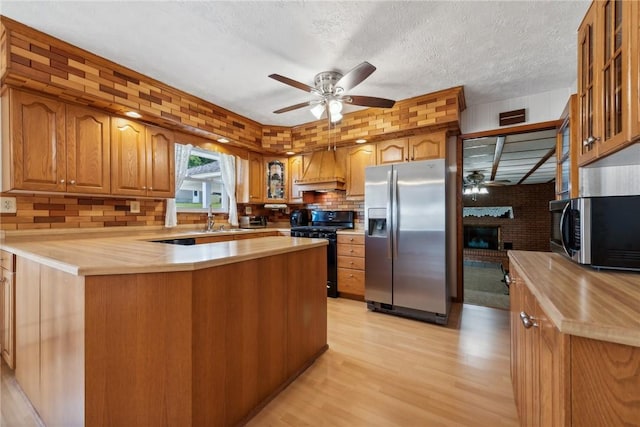 kitchen featuring ceiling fan, light hardwood / wood-style flooring, premium range hood, a textured ceiling, and appliances with stainless steel finishes