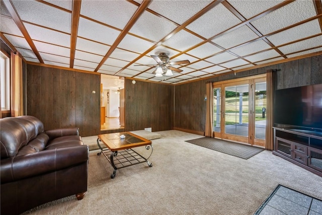 living room with carpet, ceiling fan, wood walls, and coffered ceiling