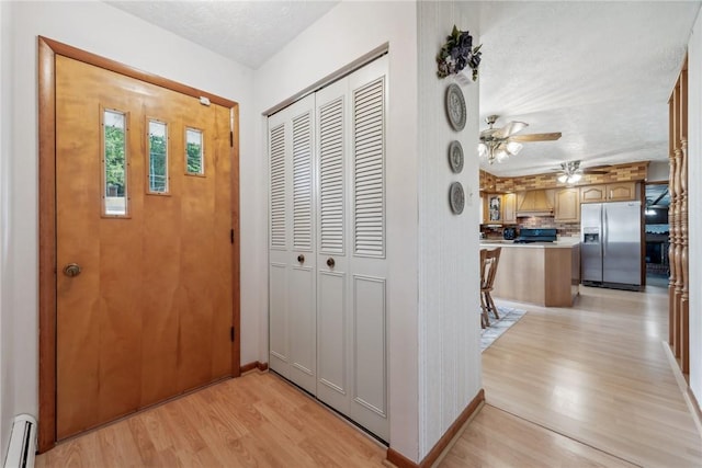 hall with a textured ceiling, a baseboard radiator, and light hardwood / wood-style flooring