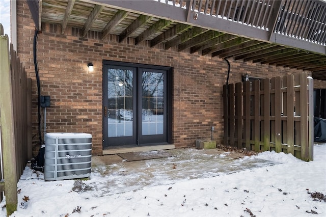 snow covered property entrance with central air condition unit and french doors