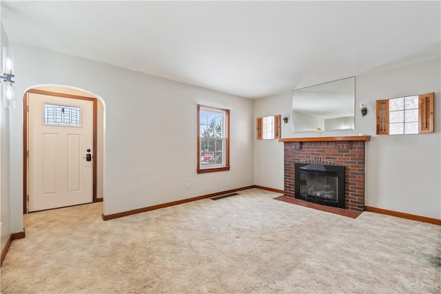 unfurnished living room featuring light carpet and a brick fireplace