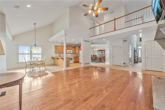 unfurnished living room with ceiling fan with notable chandelier, light hardwood / wood-style flooring, and high vaulted ceiling