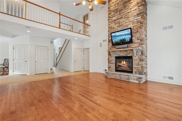 unfurnished living room with ceiling fan, a fireplace, a high ceiling, and light wood-type flooring