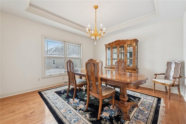 dining space featuring light hardwood / wood-style floors, an inviting chandelier, and a tray ceiling