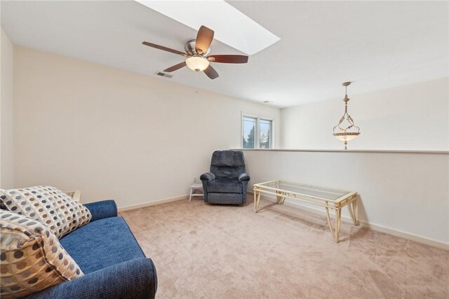 living area with ceiling fan, light colored carpet, and a skylight