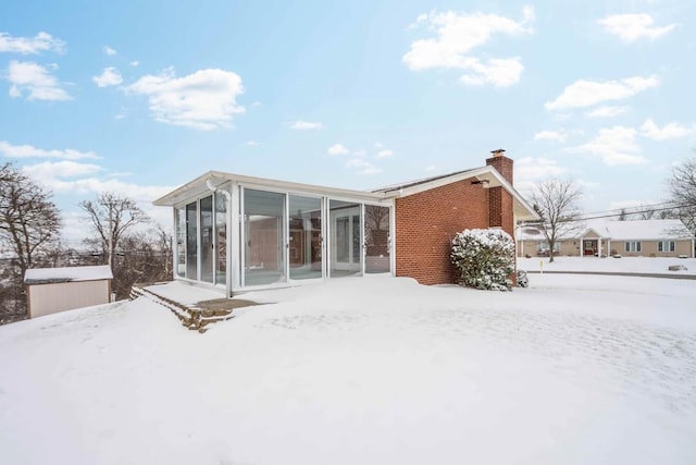 snow covered rear of property with a sunroom