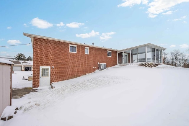 snow covered rear of property with central air condition unit and a sunroom