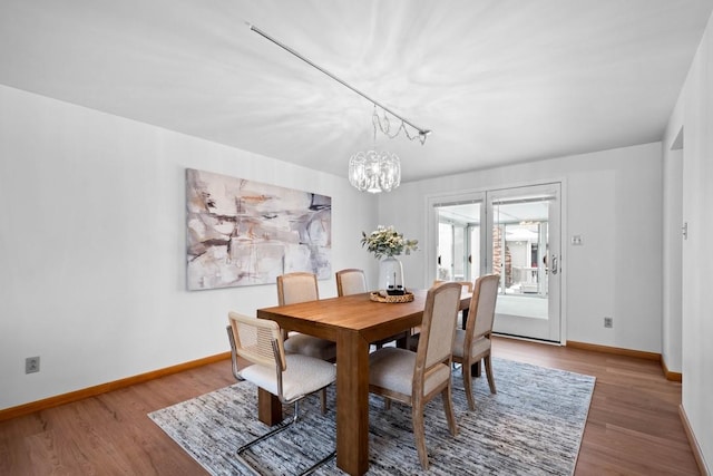 dining space with track lighting, hardwood / wood-style flooring, and an inviting chandelier