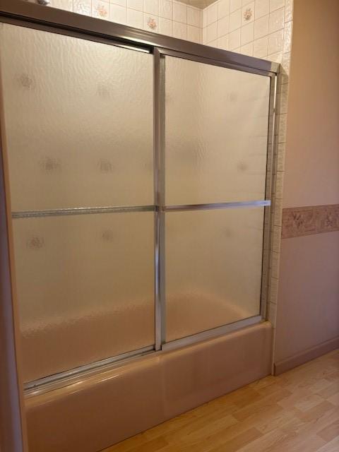 bathroom featuring wood-type flooring and shower / bath combination with glass door