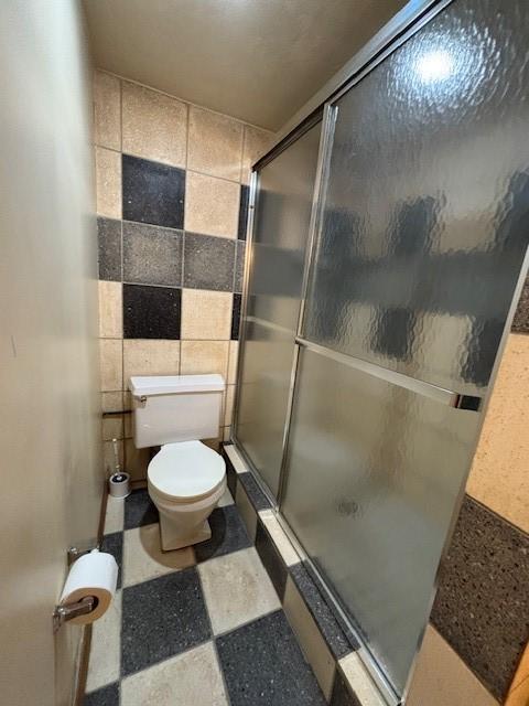 bathroom featuring tile walls, an enclosed shower, and toilet