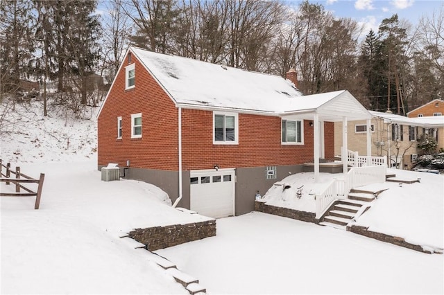 snow covered house with a garage and central AC unit