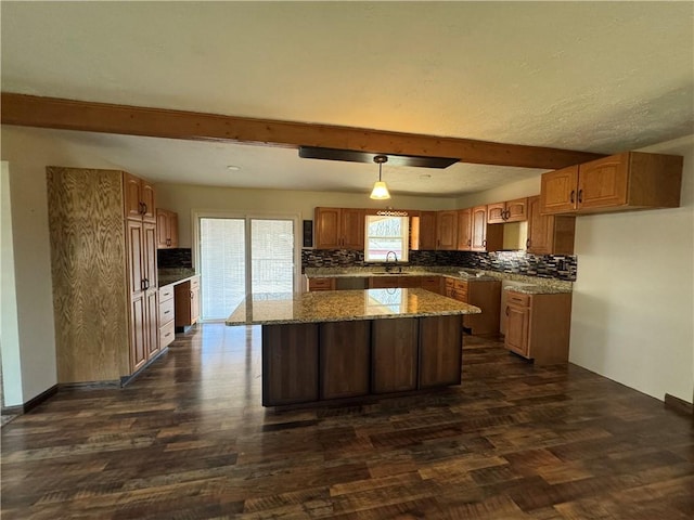 kitchen featuring light stone counters, sink, decorative light fixtures, beamed ceiling, and a kitchen island