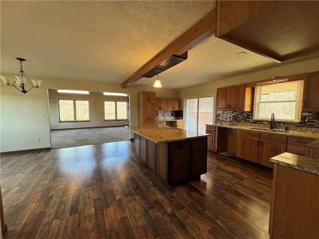 kitchen with sink, hanging light fixtures, beam ceiling, a notable chandelier, and a kitchen island