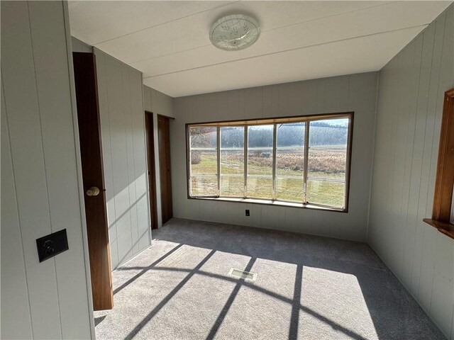 carpeted spare room featuring wood walls