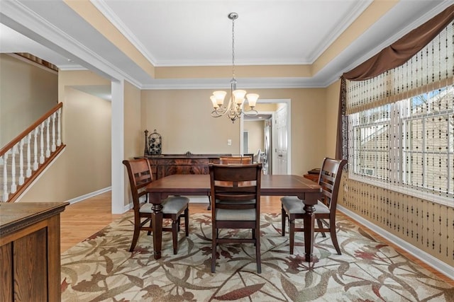 dining area with light wood-type flooring, ornamental molding, a tray ceiling, and a chandelier