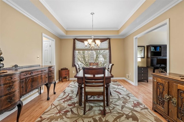 dining room with a tray ceiling, crown molding, a notable chandelier, and light hardwood / wood-style floors