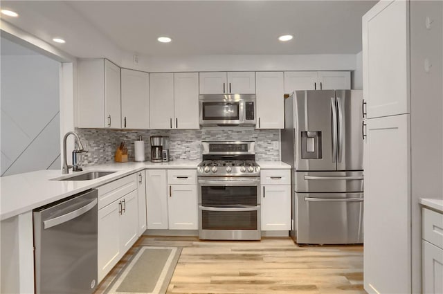 kitchen featuring backsplash, sink, appliances with stainless steel finishes, light hardwood / wood-style floors, and white cabinetry