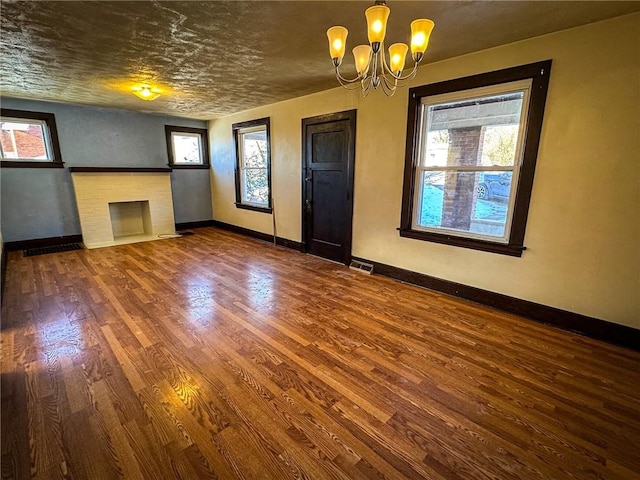 unfurnished living room with a fireplace, a notable chandelier, wood finished floors, and baseboards