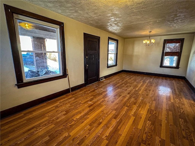 unfurnished room with dark wood finished floors, a textured ceiling, baseboards, and a chandelier