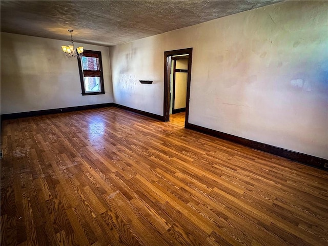 unfurnished room with baseboards, a textured ceiling, an inviting chandelier, and dark wood-style flooring