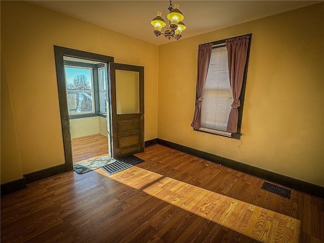 spare room with baseboards, wood finished floors, visible vents, and a chandelier