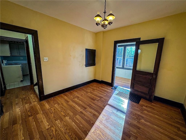 unfurnished room featuring baseboards, wood finished floors, and a chandelier