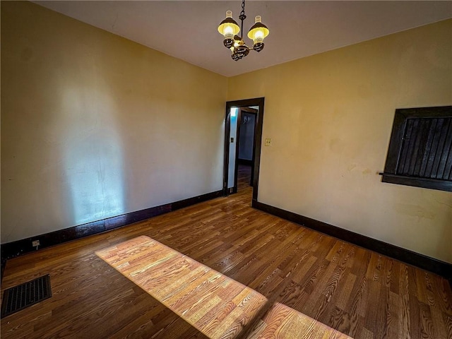 empty room featuring an inviting chandelier, wood finished floors, baseboards, and visible vents