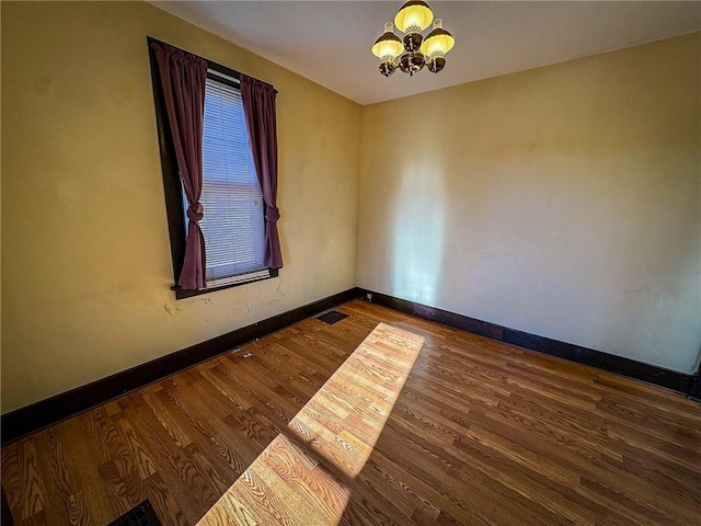 spare room featuring dark hardwood / wood-style flooring and a chandelier